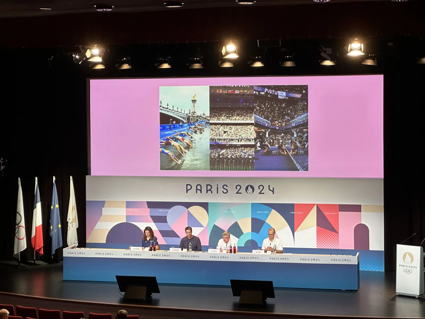 Pressekonferenz auf einer Bühne mit großer Leinwand